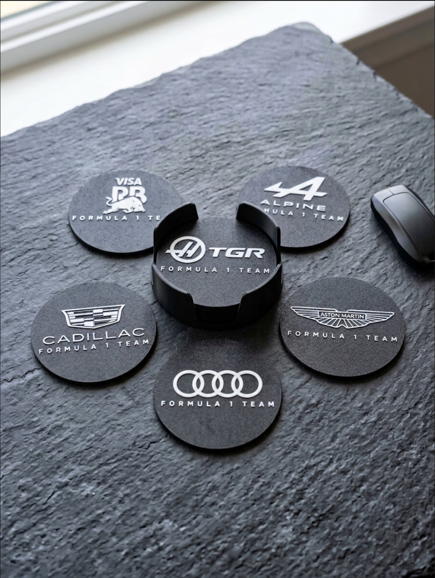 Close-up of Formula 1 team logo coasters set with 3D printed holder on textured surface